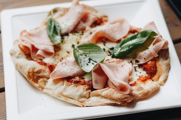 Fresh baked pizza with melted cheese Italian herbs and tomato sauce and fresh basil on a white plate on a kitchen background selective focus