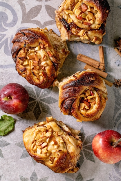 Photo fresh baked sweet apple sticky cinnamon rolls buns with gardening apples and cinnamon sticks on ornate ceramic tile background. traditional home bakery