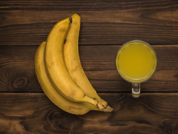 Fresh bananas and a glass of banana smoothie on a wooden table Flat lay