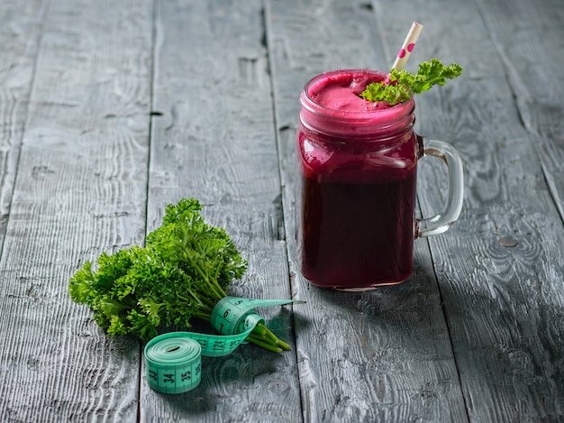 Fresh beetroot smoothie, measuting tape, two beet and parsley on black wooden table