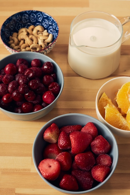 Fresh berries orange nuts in bowls and milk in jug