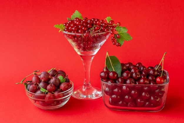 Fresh berries red currants gooseberries cherries in a glass container on a red background