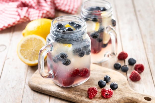 Fresh berry drink with blueberries and raspberries and lemon on wooden tablexA