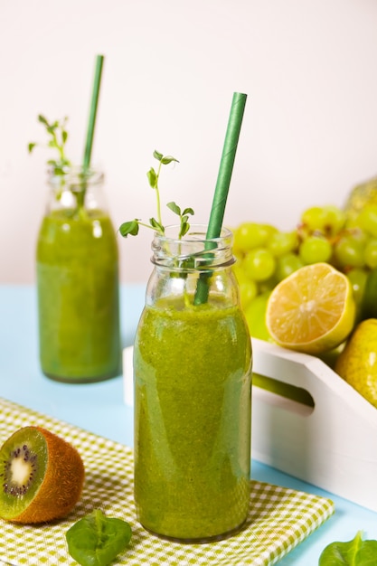 Fresh blended green smoothie in glass small bottles with fruit and vegetables . Health and detox concept.