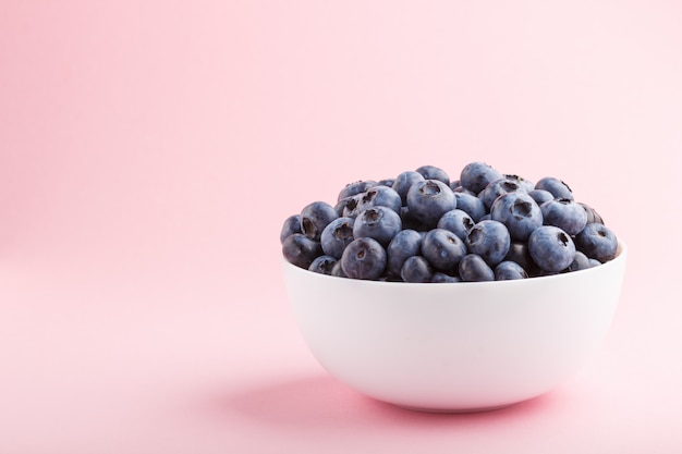 Fresh blueberry in white bowl on  pink background. side view.