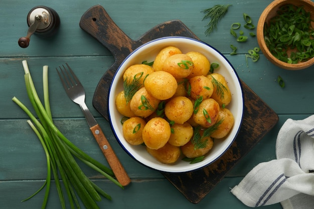 Fresh boiled new or young potatoes with butter fresh dill and onions in white bowl on old rustic wooden background Tasty new boiled potatoes Top view