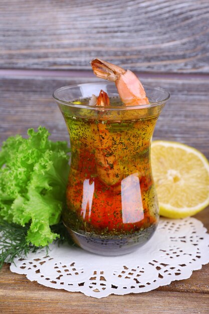 Fresh boiled prawns with lettuce and lemon in a glass of sauce on a lace napkin on wooden background