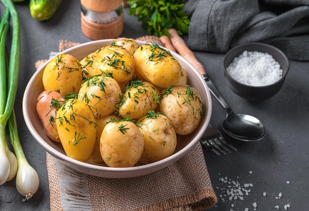 Fresh boiled young unpeeled potatoes with dill and butter on a dark background with dill and spices