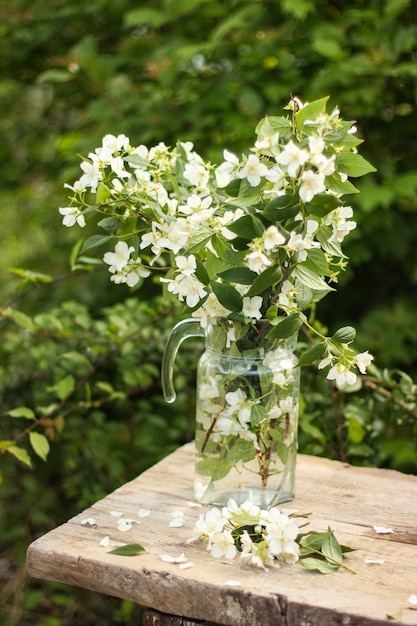 fresh bouquet of blooming fragrant jasmine in a glass vase in rustic style on an old wooden table