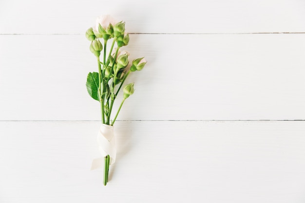 Fresh bouquet of small pink roses with buds with white ribbon.Minimalist flat lay,white wooden background.