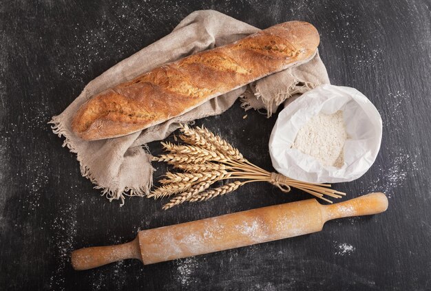 Fresh bread with wheat ears flour and kitchen utensils on dark board