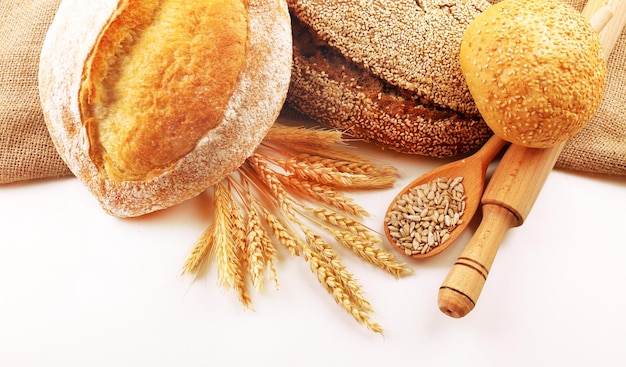 Fresh bread with wheat and wooden spoon of sunflower seeds isolated on white