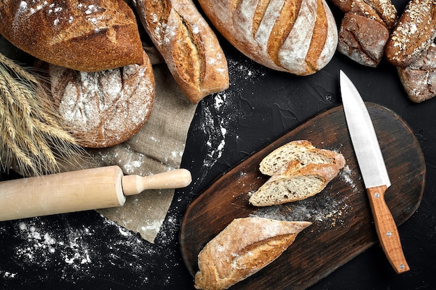 Fresh bread wooden board and cutting knife on black table