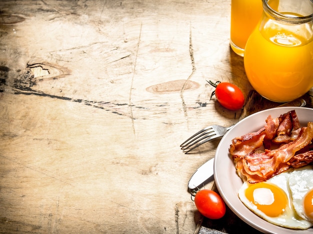 fresh Breakfast. Orange juice with fried eggs, bacon, and slices of bread. On a wooden table.