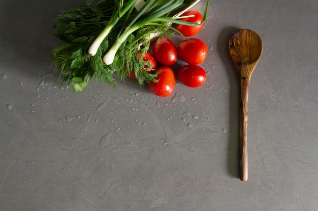 Fresh bright fragrant vegetables and a bamboo spoon lie on the gray kitchen