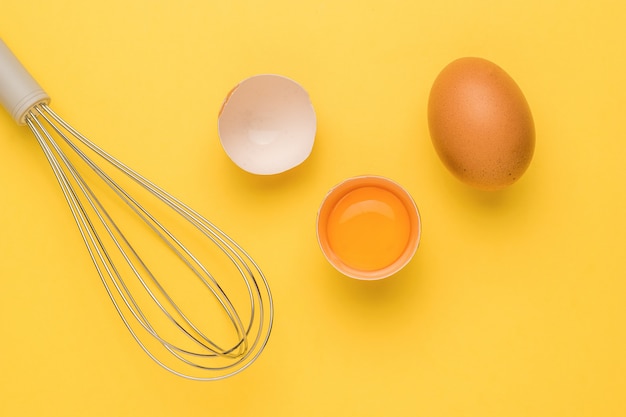 Fresh brown eggs and a whisk for whipping on a yellow background.