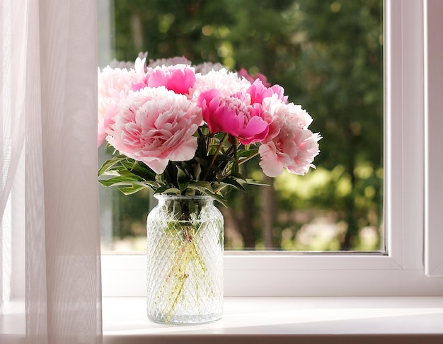 Fresh bunch of pink peonies in a glass vase on the windowsill