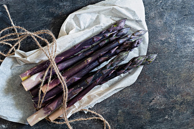 Fresh bunch of purple asparagus on packaging paper on a dark wooden background Healthy food concept