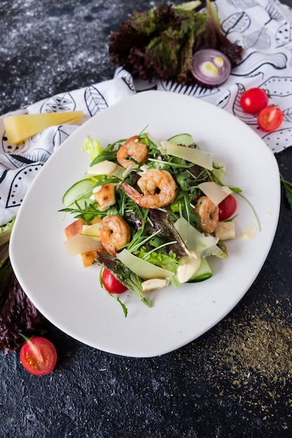 Fresh caesar salad with shrimps on white plate on dark stone. 