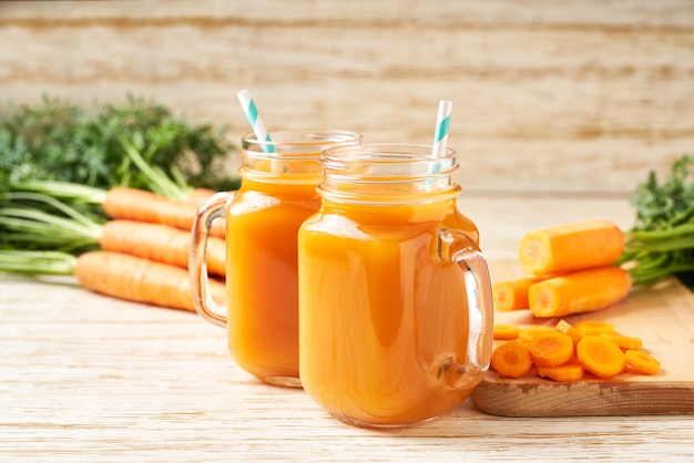 Fresh carrot juice in a mason jar glass. Scene with ingredients against a wooden table. 