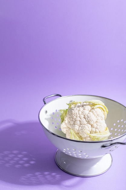 Fresh cauliflower in a colander on a purple background with hard shadows, copy space.