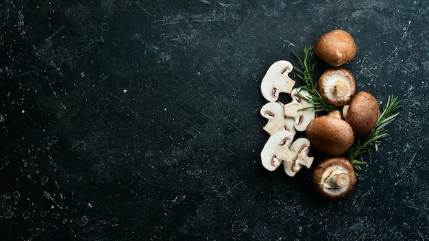 Fresh champignon mushrooms on a black stone background. Rustic style. Top view.