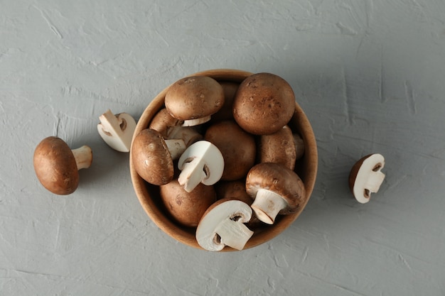 Fresh champignon mushrooms in bowl on grey, top view