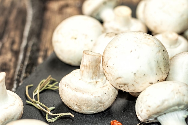 Fresh champignons with spices and herbs. Raw ingredient for cooking vegan food. Old wooden background, fashion hard light, dark shadow, rustic style, close up