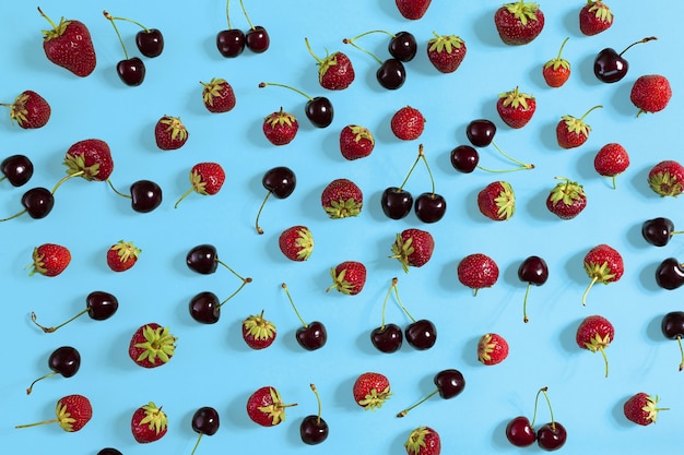 Fresh cherries and strawberries on blue background, top view. Copy space. Flat lay