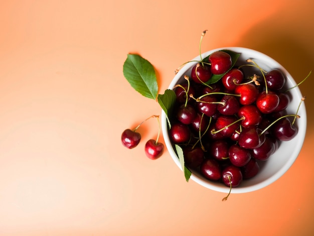 Fresh cherries in a white bowl on an orange background with place for text