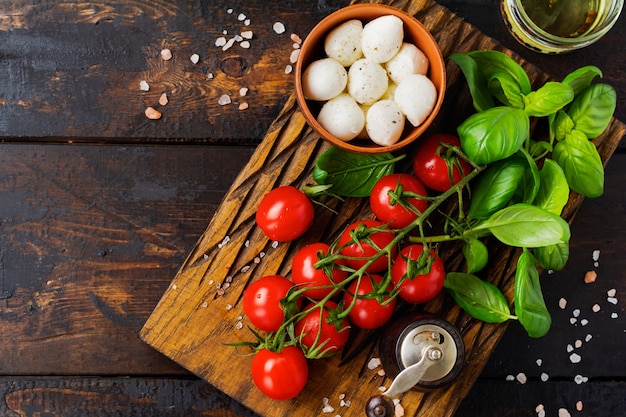 Fresh cherry tomatoes, basil leaves, mozzarella cheese and olive oil on old wooden surface. Caprese salad ingredients. Selective focus.