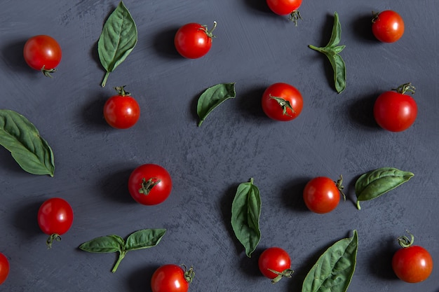 Fresh cherry tomatoes with basil leaves on a black background.