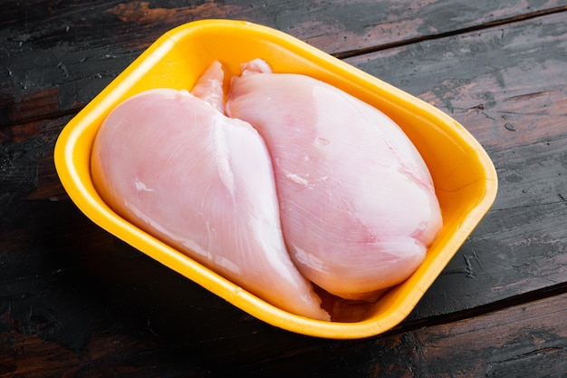 Fresh chicken breast meat in open tray, on dark wooden background