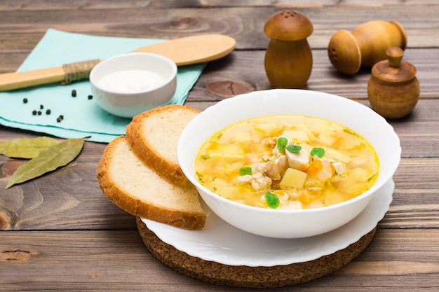 Fresh chicken broth soup with potatoes and herbs in a white bowl on a wooden table