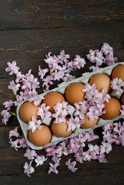 Fresh Chicken brown eggs in carton box on wooden table. organic farming concept. Natural healthy food. eggs in tray and flowers. Moody Easter