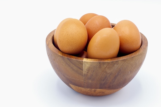 Fresh chicken eggs in a wooden bowl on a white background