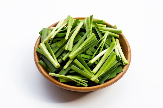 Fresh Chinese Chive leaves in wooden bowl on white.