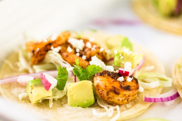 Fresh chipotle shrimp tacos with cotija cheese on a white corn tortillas.