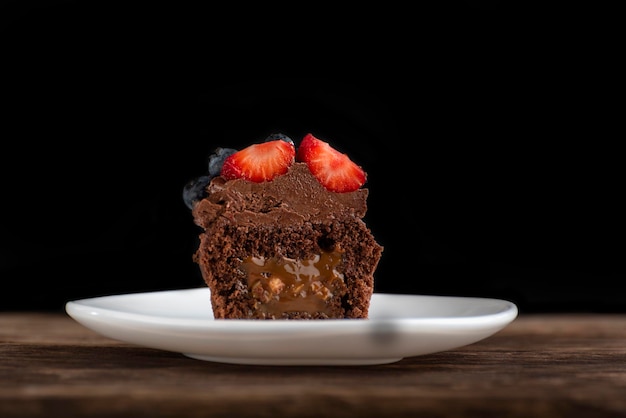 Fresh chocolate muffin with berries Half chocolate cupcake with filling in cut on wooden surface on black background