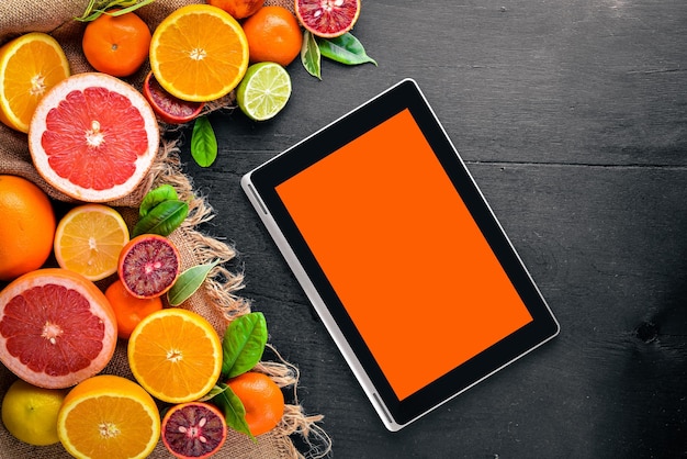 Fresh citrus fruits on a table with a laptop. Lemon orange, tangerine, lime. On a black background Wooden. Top view.