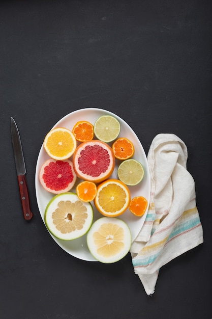 Fresh citrus fruits on white dish close up, dark background