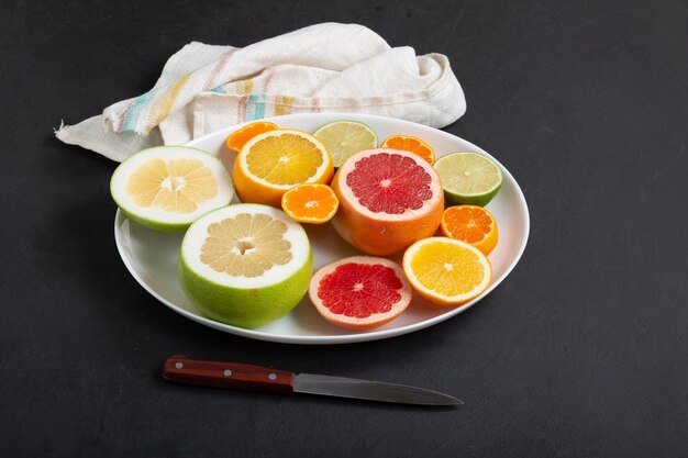 Fresh citrus fruits on white dish close up, dark background