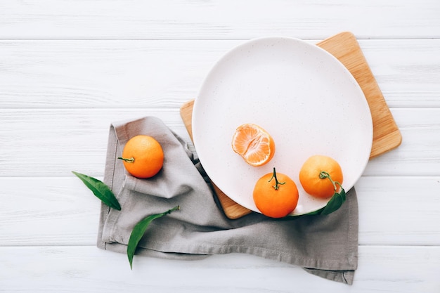 Fresh clementines with leaves, plate, cutting board on wooden table.