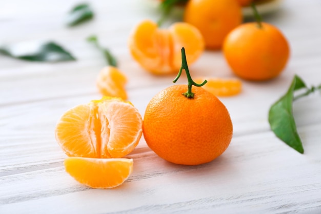 Fresh clementines with leaves on white wooden table.