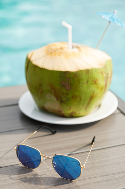 Fresh coconut drink and sunglasses on the table beside the swimming pool