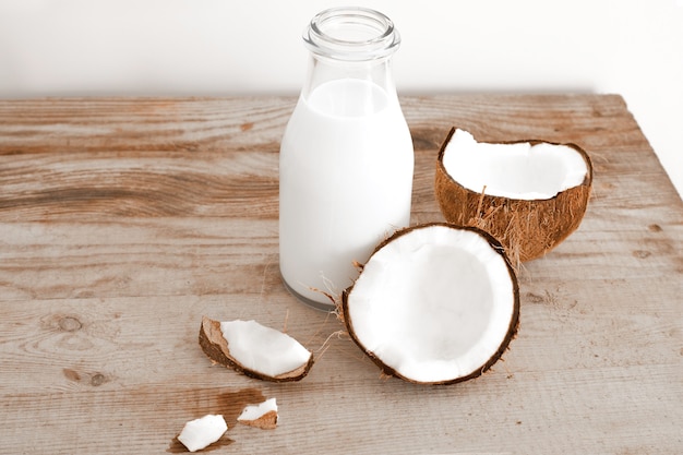 Fresh coconut milk in glass bottle, vegan non dairy healthy drink. Wooden table, close-up.