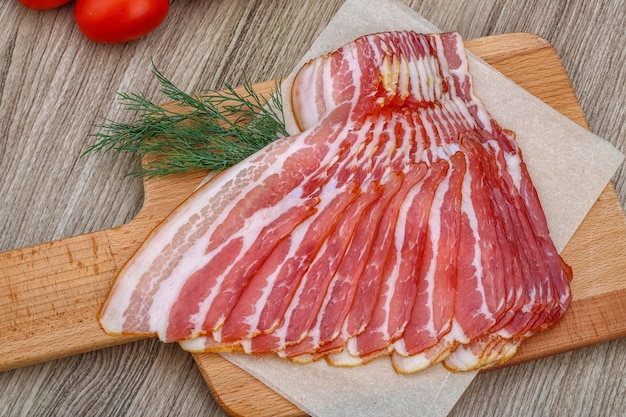 Fresh cold sliced bacon with dill branch on the wood background