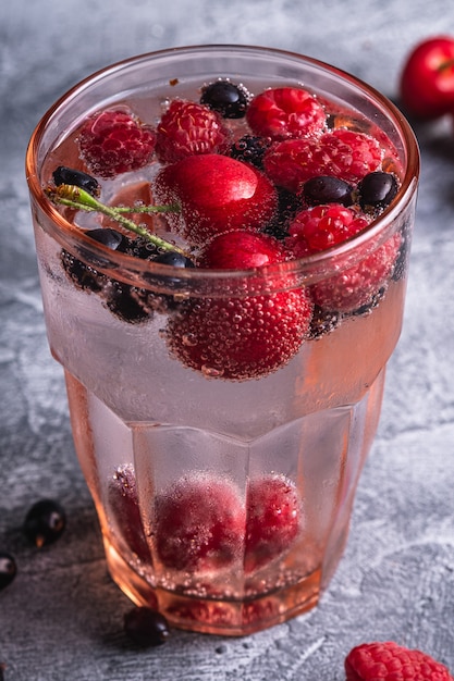 Fresh cold sparkling water drink with cherry, raspberry and currant berries in red faceted glass