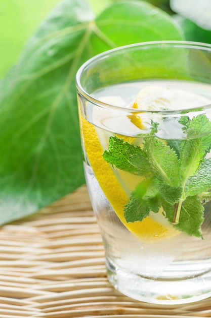 Fresh Cool Infused Detox Water with Sliced Lemons, Mint in Frosty Glass on Wicker Table.