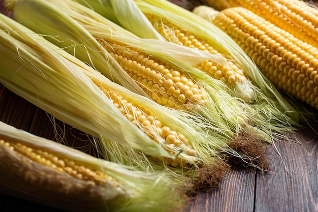 Fresh corn cobs on rustic wooden table close up Top view